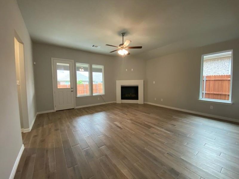 Spacious interior room featuring wood-finish flooring, a contemporary fireplace with a white mantel, and a ceiling fan with integrated lighting Spacious interior room featuring wood-finish flooring, a contemporary fireplace with a white mantel, and a ceiling fan with integrated lighting