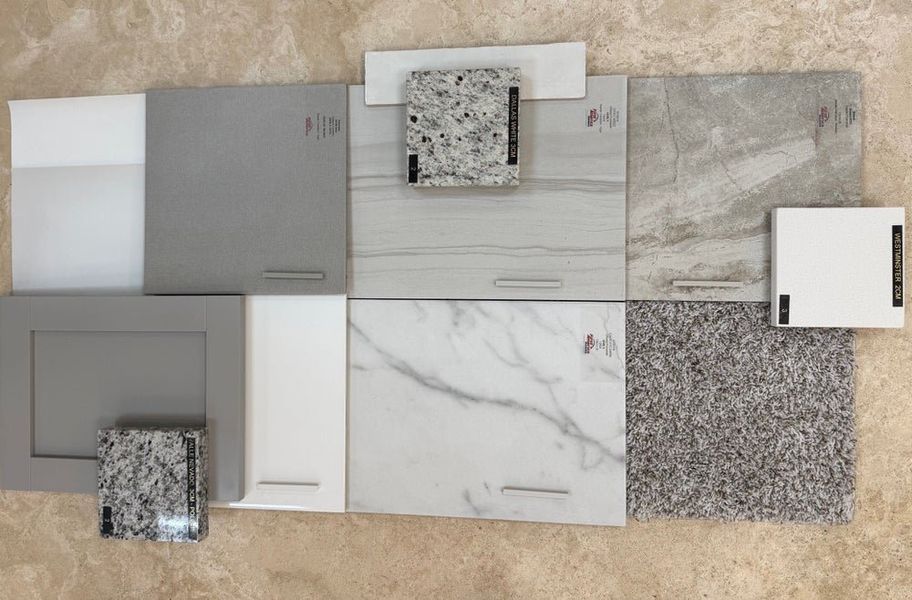 Home design material samples including gray and white cabinet doors, granite countertop swatches, marble tile, and carpet samples arranged flat. Home design material samples including gray and white cabinet doors, granite countertop swatches, marble tile, and carpet samples arranged flat.