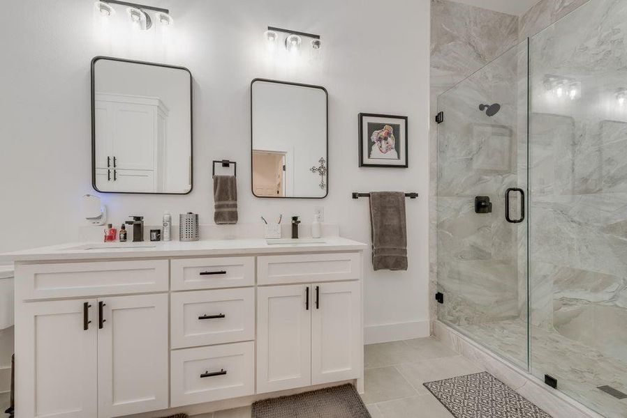 Full bath featuring double vanity, a marble finish shower, and light tile patterned floors