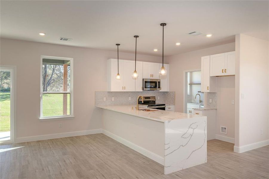 Kitchen featuring appliances with stainless steel finishes, decorative light fixtures, white cabinets, kitchen peninsula, and light hardwood / wood-style flooring