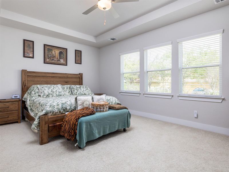 Primary Bedroom with light carpet, a tray ceiling, and ceiling fan
