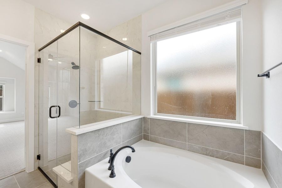 Bathroom with soaking tub, glass-enclosed shower, gray tile surround, and frosted privacy window