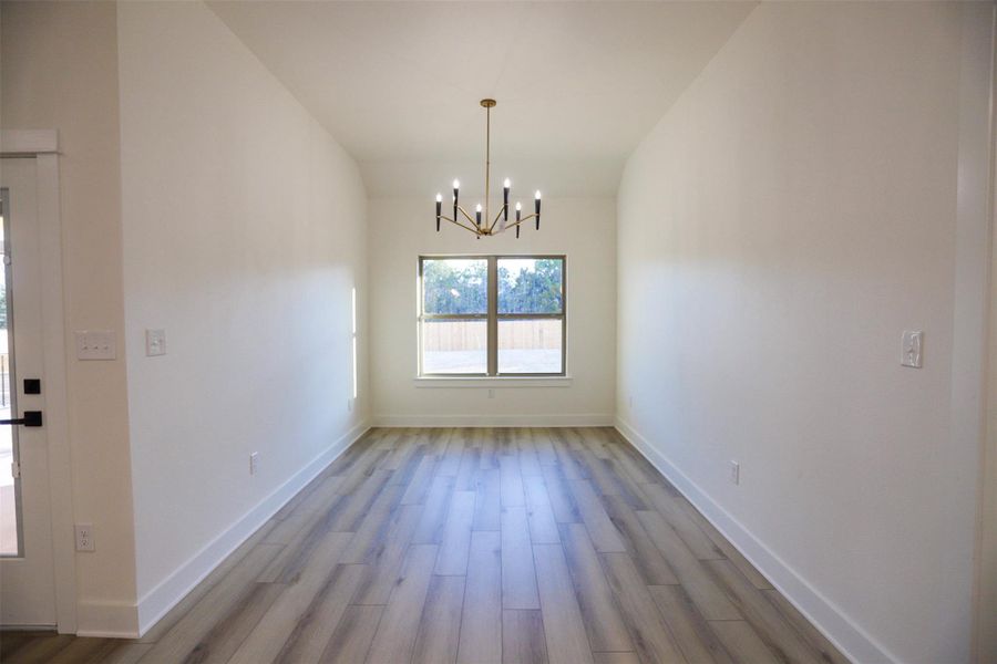Unfurnished dining area featuring hanging lights, light wood-style flooring, and vaulted ceiling