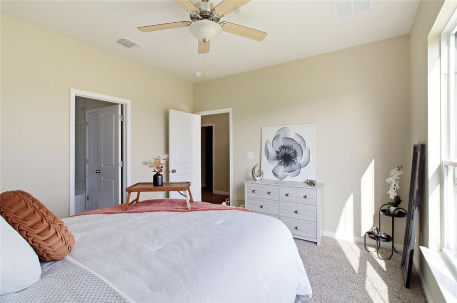 A well-lit bedroom with soft carpet flooring and a ceiling fan for comfort.