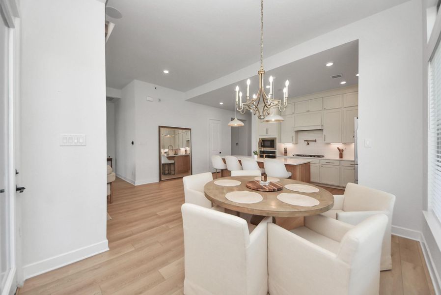 Bright and inviting dining area with a round table, plush chairs, and an elegant chandelier, seamlessly flowing into a modern kitchen with sleek cabinetry and stainless steel appliances.