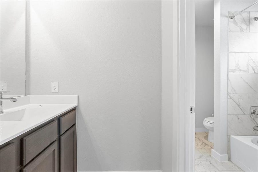 Secondary bath features a private vanity area and then opens to a shared tub/shower combo and toilet. Features include tile flooring, bath/shower combo with tile surround, wood stained cabinets, beautiful light countertops, mirror, dark, sleek fixtures and modern finishes!