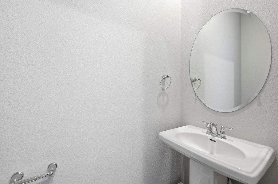 White pedestal sink with chrome faucet, complemented by a large oval mirror and chrome towel rings White pedestal sink with chrome faucet, complemented by a large oval mirror and chrome towel rings