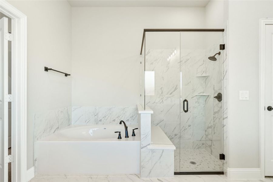 Bathroom with soaking tub and glass walk-in shower, both featuring white marble tile and dark bronze fixtures Bathroom with soaking tub and glass walk-in shower, both featuring white marble tile and dark bronze fixtures