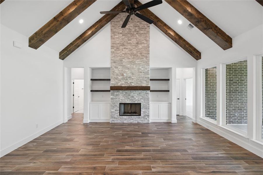 Unfurnished living room featuring high vaulted ceiling, beamed ceiling, built in shelves, and a stone fireplace