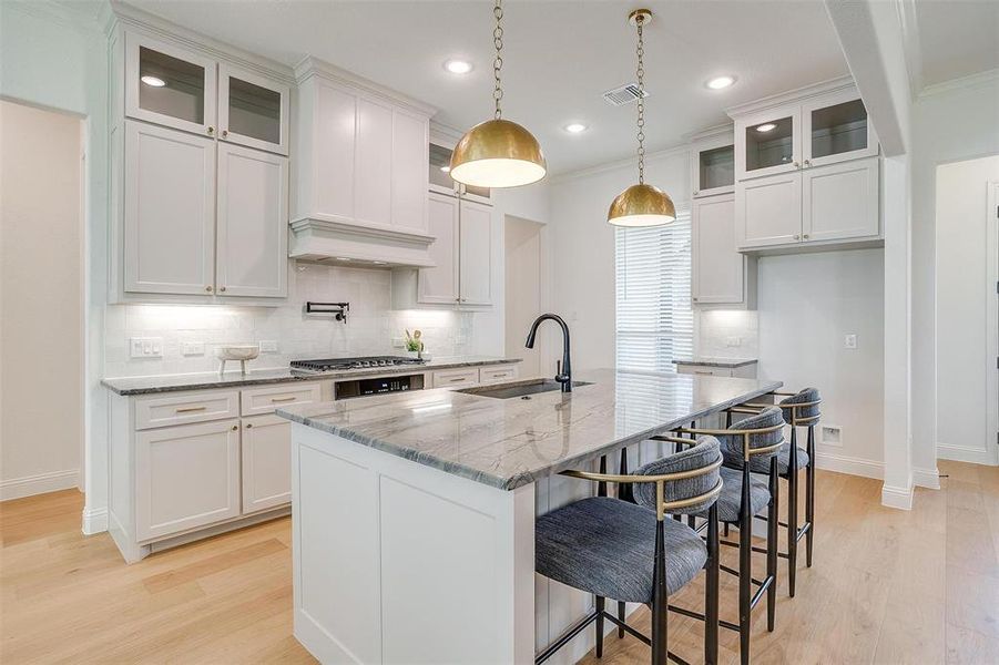 Kitchen with premium range hood, light hardwood / wood-style floors, tasteful backsplash, and sink