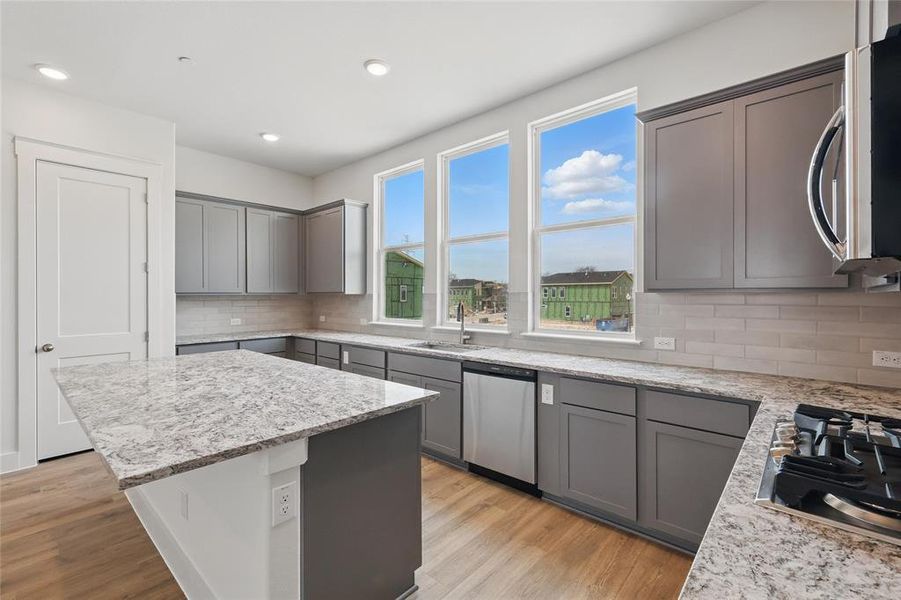 Kitchen featuring gray cabinetry, light wood finished floors, stainless steel appliances, light stone countertops, and recessed lighting