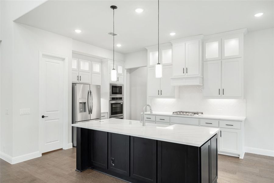White kitchen with black island, quartz countertops, stainless appliances, and pendant lights over dark hardwood floors White kitchen with black island, quartz countertops, stainless appliances, and pendant lights over dark hardwood floors