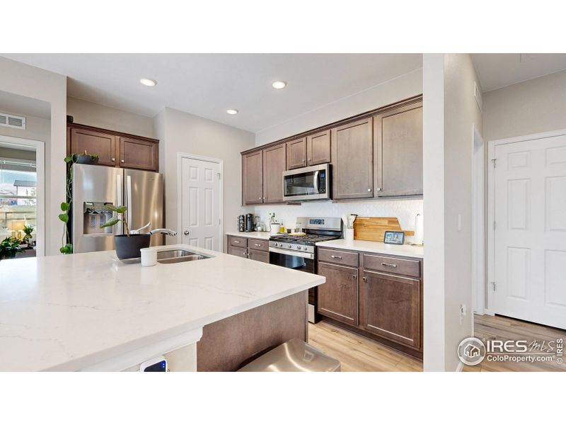 Spacious kitchen featuring stainless steel appliances, a gas range and oven, quartz countertops including a kitchen island and a custom tile backsplash.