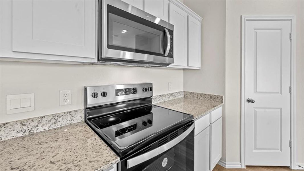 Kitchen with stainless steel appliances, light stone countertops, and white cabinetry
