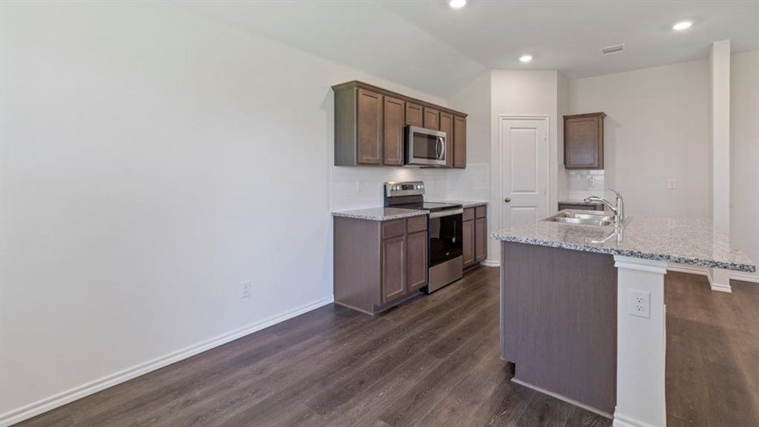 Kitchen featuring wood-finish flooring, dark wood cabinetry, stainless steel appliances, speckled stone countertops, and a white subway tile backsplash
