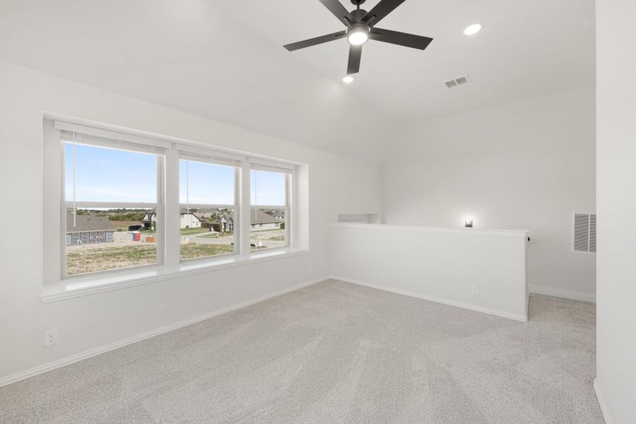 Empty upstairs bonus room with carpet, ceiling fan, and large windows overlooking a neighborhood