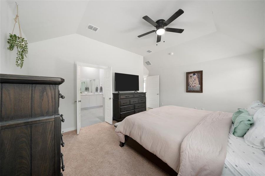 Bedroom with ensuite bathroom, ceiling fan, lofted ceiling, and light colored carpet