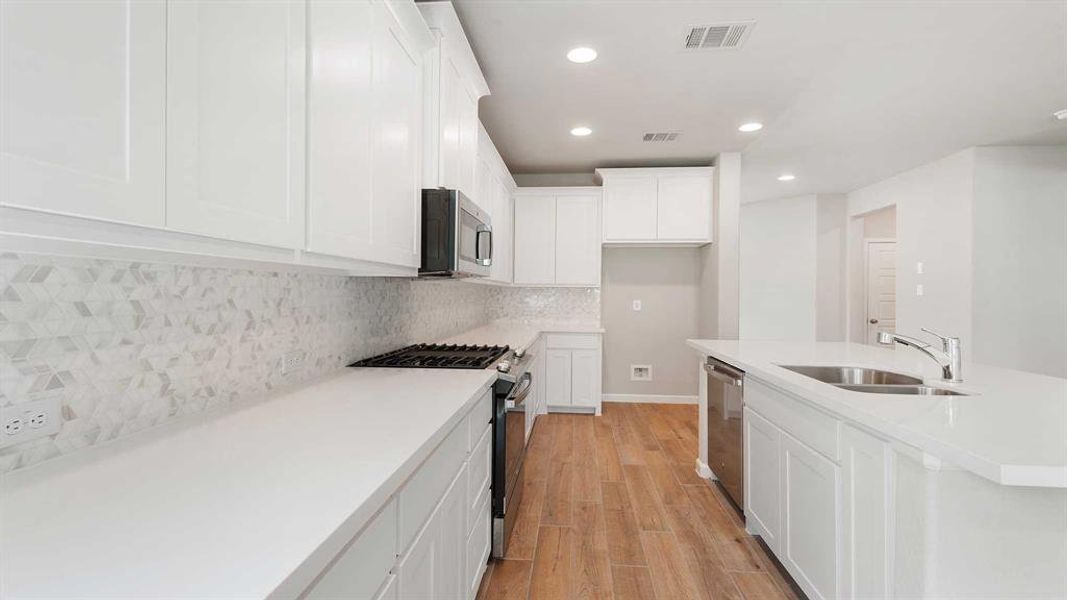 Kitchen featuring appliances with stainless steel finishes, tasteful backsplash, white cabinets, sink, and light hardwood / wood-style floors