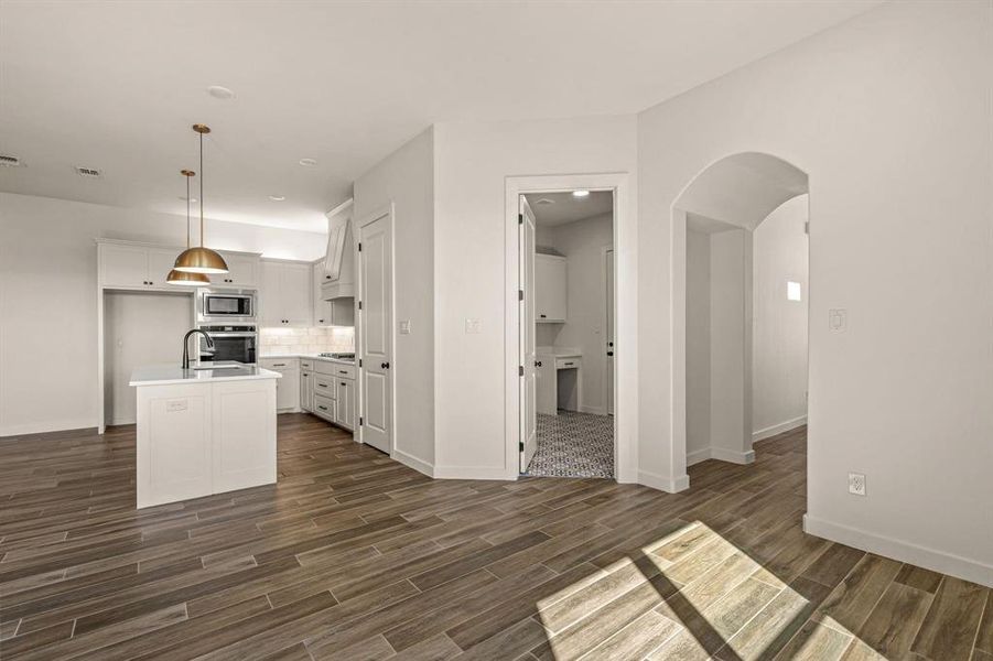 Kitchen with appliances with stainless steel finishes, dark wood-style flooring, light countertops, a center island with sink, and backsplash