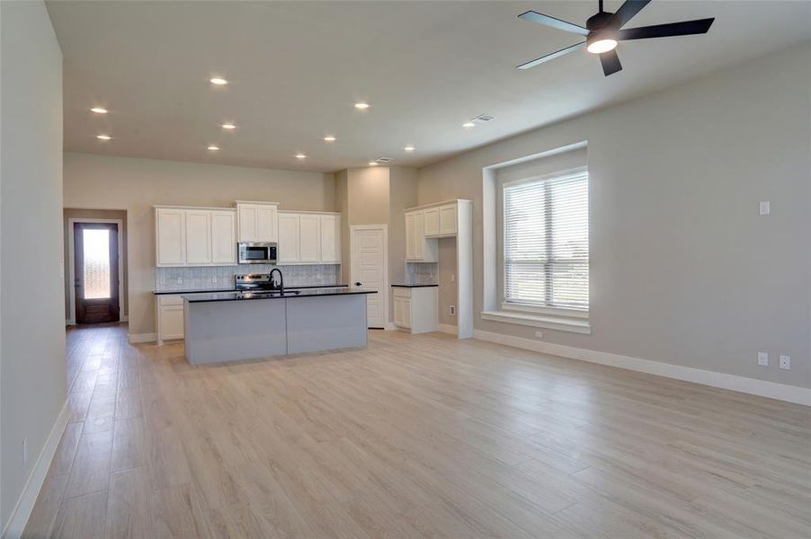 Kitchen featuring dark countertops, white cabinetry, open floor plan, backsplash, and recessed lighting Kitchen featuring dark countertops, white cabinetry, open floor plan, backsplash, and recessed lighting
