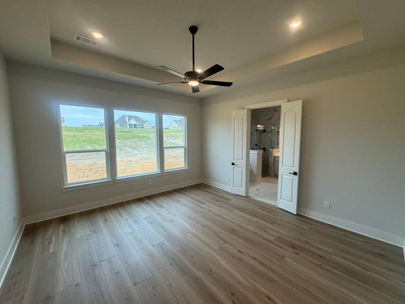 Spacious room featuring wood-finish flooring, a tray ceiling with recessed lighting and a ceiling fan, and a three-panel window overlooking the exterior Spacious room featuring wood-finish flooring, a tray ceiling with recessed lighting and a ceiling fan, and a three-panel window overlooking the exterior
