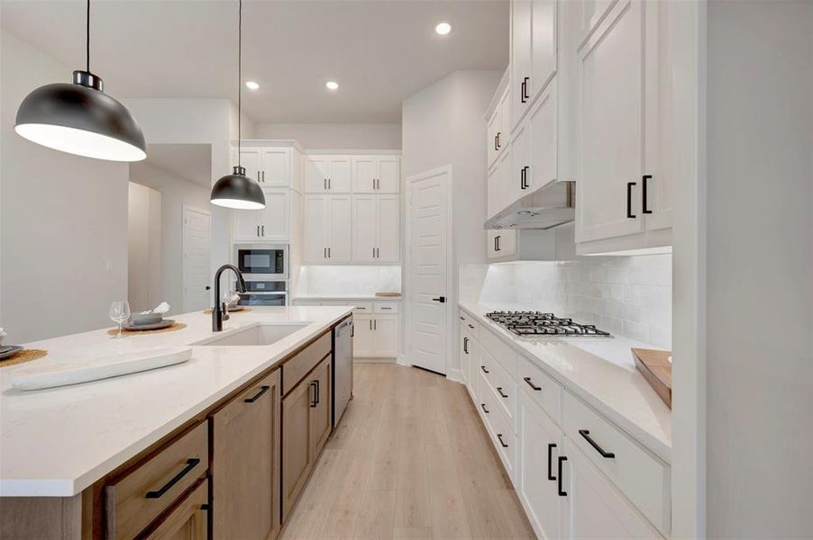 Dual tone kitchen featuring two tone cabinetry, backsplash, light stone counters, light wood-style flooring, and an island with sink