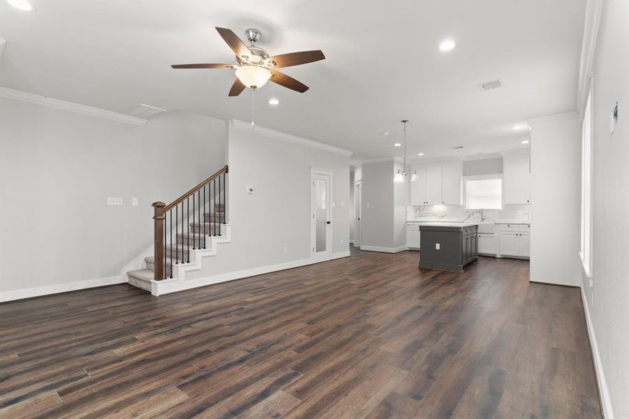 This is a spacious, open-concept interior featuring a modern kitchen with white cabinetry and quartz countertops, Laminate wood floors, a staircase with wooden banisters, and ample natural light. A ceiling fan adds comfort to the main living area.