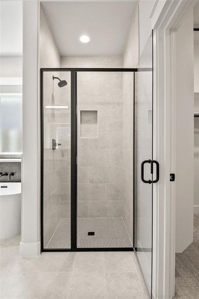 Spacious walk-in shower featuring a frameless glass enclosure with matte black trim, subway tile walls, a built-in shower niche, and a contrasting penny tile floor