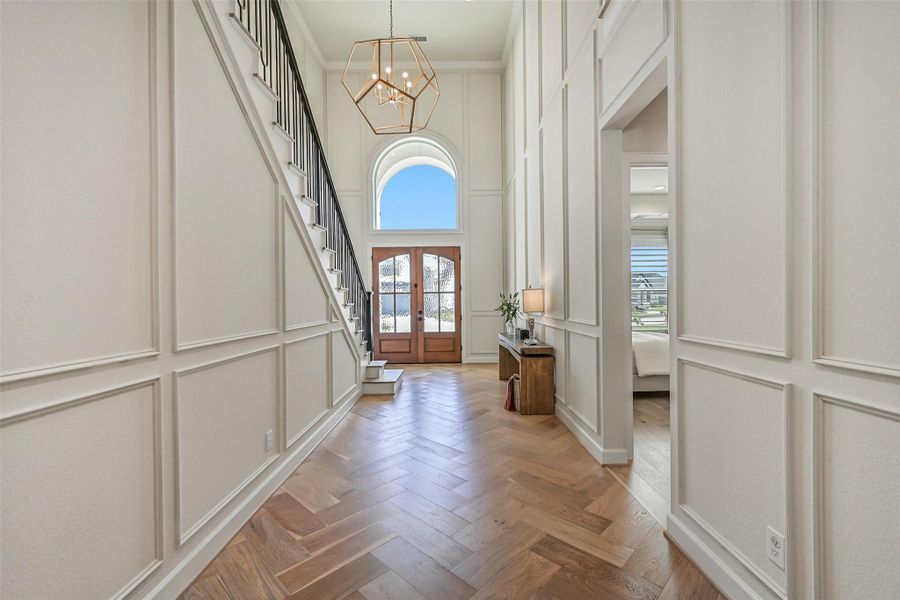 Looking back toward the entry showcases the impressive 20' ceiling, with custom molding extending from floor to ceiling, herringbone wood-look tile & an oversized arched window above the double entry doors flooding the foyer with natural light.