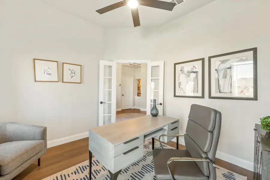 Home office with wood desk, leather chair, hardwood floors, and French doors with glass panels