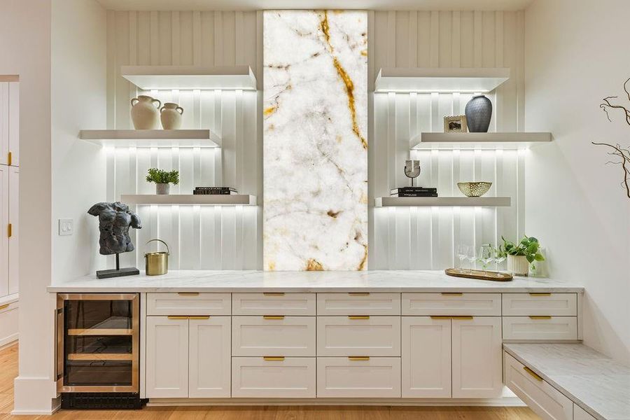 Experience the perfect marriage of architectural grandeur and cozy refinement in this stunning, light-filled family room. Designed to be the heart of the home, this space is defined by its backlit onyx feature wall, which casts a warm, ethereal glow over the custom-built cabinetry and integrated wine bar—ideal for the seamless host