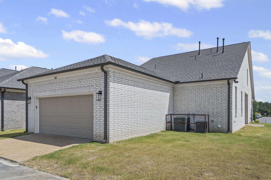 View of side of home featuring brick siding, a shingled roof, a lawn, and an attached garage