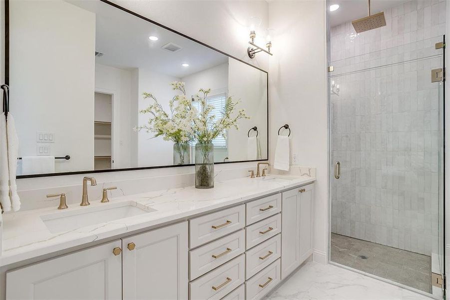 Primary Bathroom featuring vanity with dual sinks, gold hardware, tile flooring and walk in shower with two shower heads including rain fall.