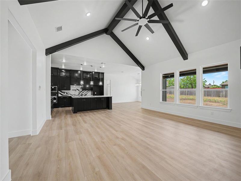 Vaulted ceiling with exposed black beams and ceiling fan, light wood-finish flooring, and a kitchen featuring black cabinetry, a white and black veined countertop, and pendant lighting Vaulted ceiling with exposed black beams and ceiling fan, light wood-finish flooring, and a kitchen featuring black cabinetry, a white and black veined countertop, and pendant lighting