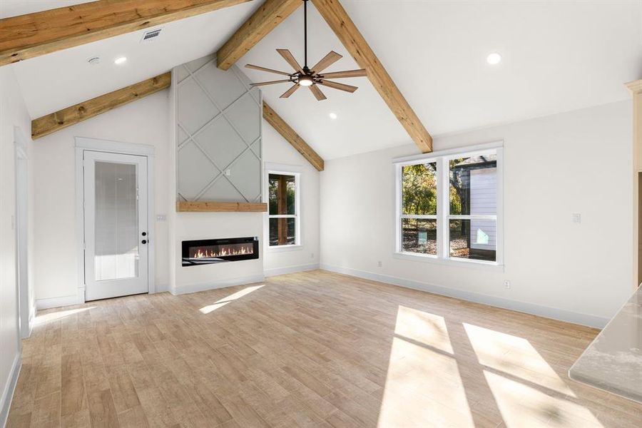 Unfurnished living room with beam ceiling, ceiling fan, light hardwood / wood-style flooring, and high vaulted ceiling