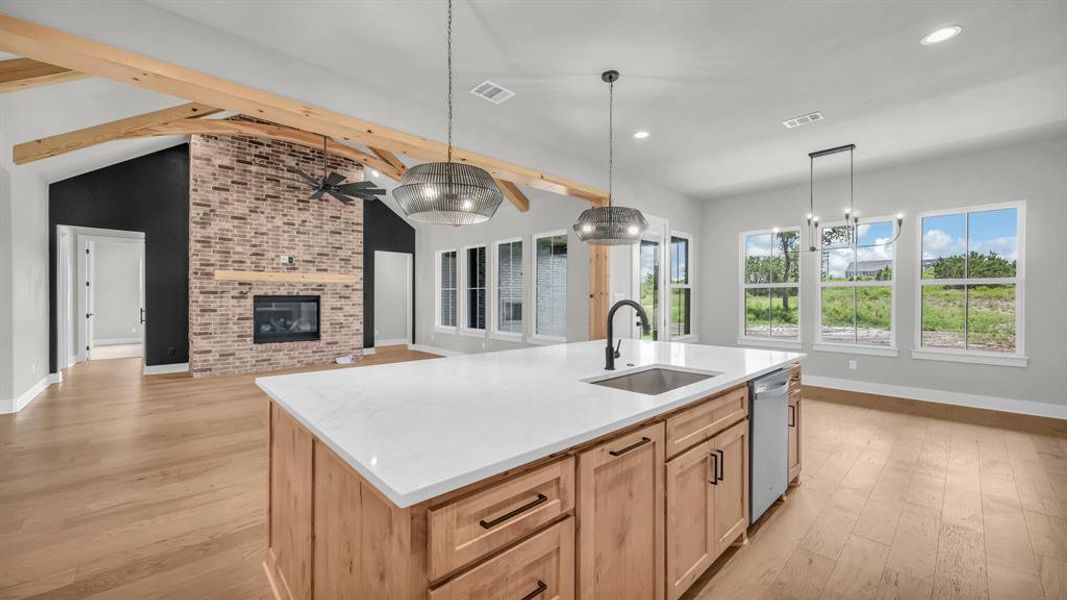 Open-concept living area featuring a kitchen island with white countertop and integrated sink, exposed wood beams, a brick fireplace, and multiple windows