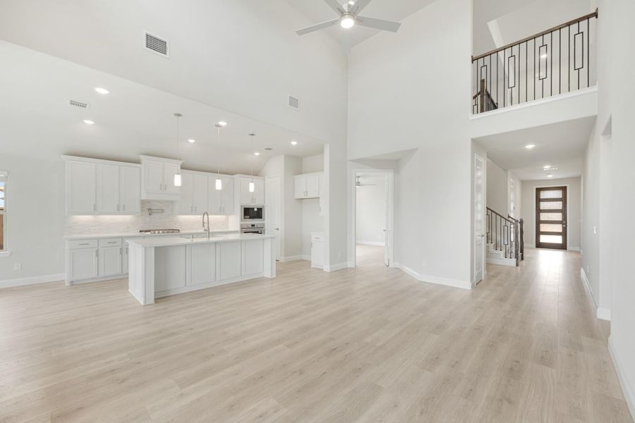 Open-concept living area with white kitchen, high ceilings, light wood floors, and staircase visible in background.
