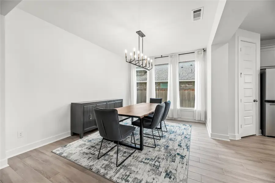 An open, light-filled dining room sets the scene for everything from elegant dinner parties to casual weeknight meals. Sleek wood-look tile flooring and a modern chandelier add style, while large windows frame the space with soft natural light.