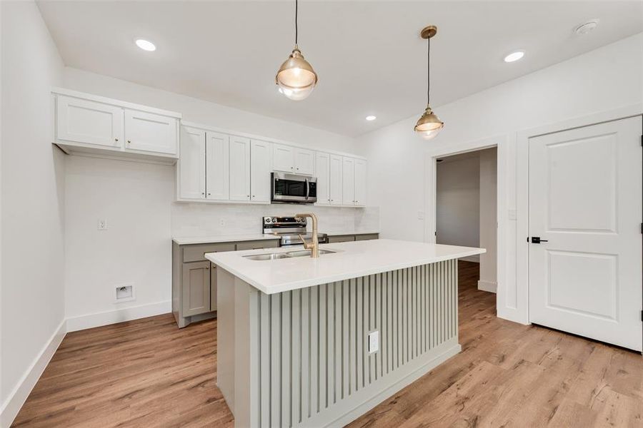 Kitchen with hanging light fixtures, white cabinetry, appliances with stainless steel finishes, light wood-style floors, and recessed lighting Kitchen with hanging light fixtures, white cabinetry, appliances with stainless steel finishes, light wood-style floors, and recessed lighting
