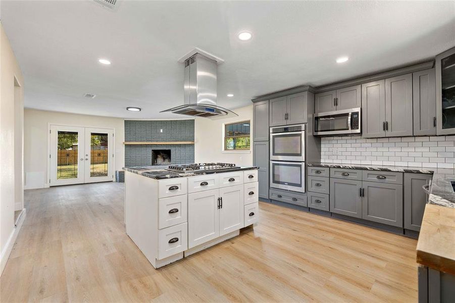Kitchen featuring gray cabinets, backsplash, island range hood, stainless steel appliances, and glass insert cabinets Kitchen featuring gray cabinets, backsplash, island range hood, stainless steel appliances, and glass insert cabinets