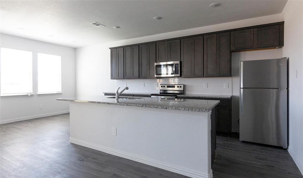 Kitchen featuring a center island with sink, sink, light stone countertops, appliances with stainless steel finishes, and dark hardwood / wood-style flooring