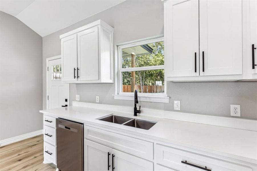 Kitchen featuring lofted ceiling, white cabinets, dishwasher, and sink