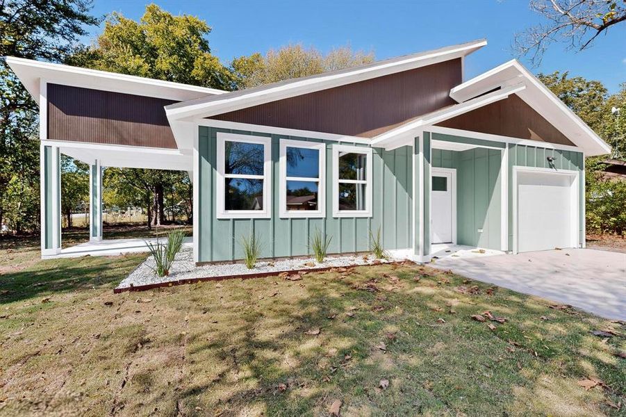 Rear view of property with a lawn, an attached garage, and board and batten siding Rear view of property with a lawn, an attached garage, and board and batten siding