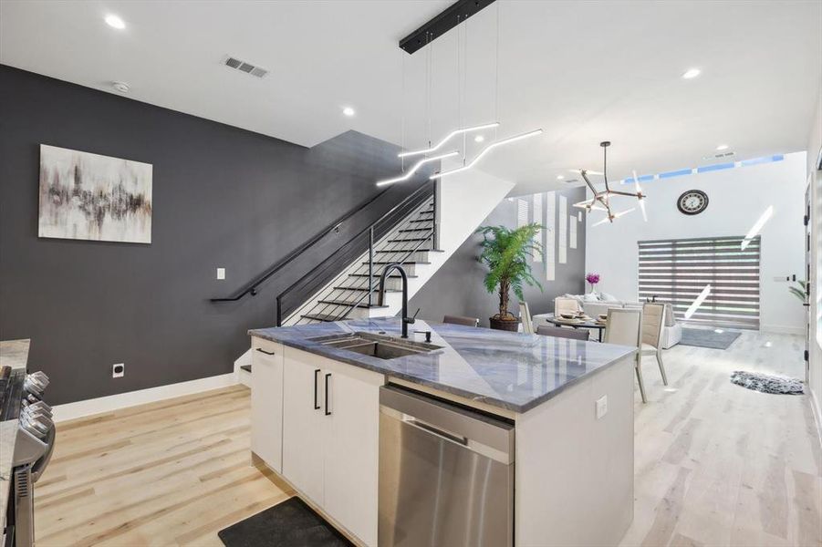 Kitchen with a center island with sink, white cabinets, stainless steel dishwasher, light hardwood / wood-style floors, and sink