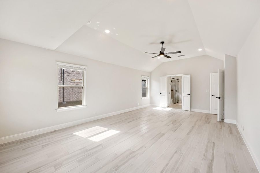 Spacious master bedroom with vaulted ceiling, ceiling fan, light wood floors, and ensuite bathroom entrance Spacious master bedroom with vaulted ceiling, ceiling fan, light wood floors, and ensuite bathroom entrance