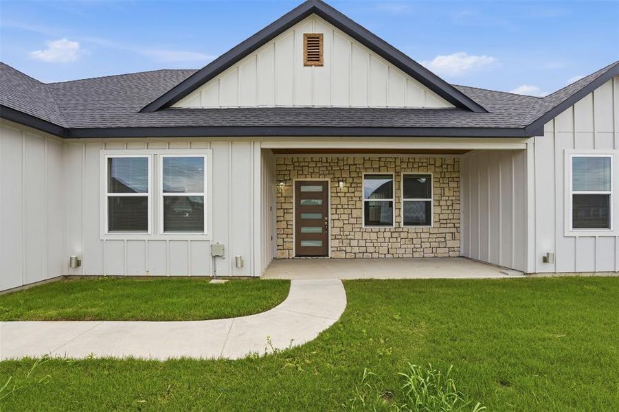 Modern farmhouse exterior featuring vertical white siding, stone accents, dark-trimmed windows, a covered entry, and a dark shingled roof