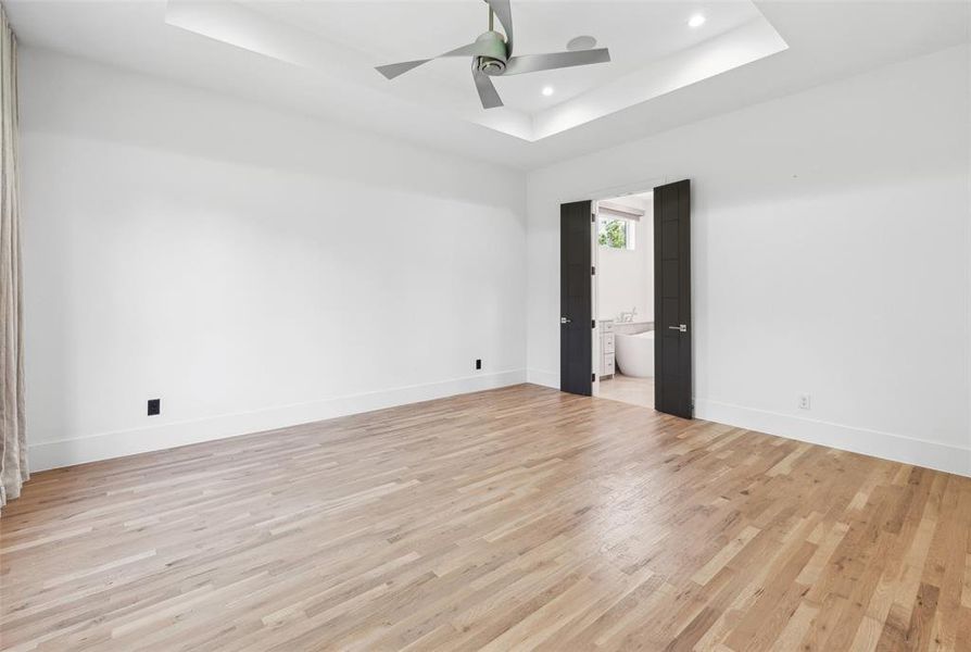 Spare room featuring ceiling fan, a tray ceiling, and light hardwood / wood-style floors