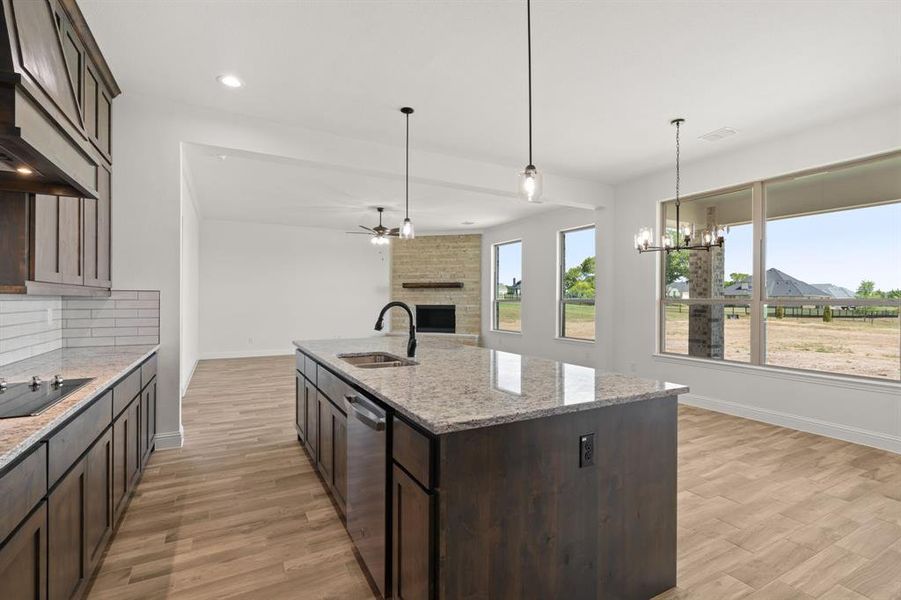 Kitchen with dark brown cabinetry, light stone counters, a kitchen island with sink, a brick fireplace, and hanging light fixtures Kitchen with dark brown cabinetry, light stone counters, a kitchen island with sink, a brick fireplace, and hanging light fixtures
