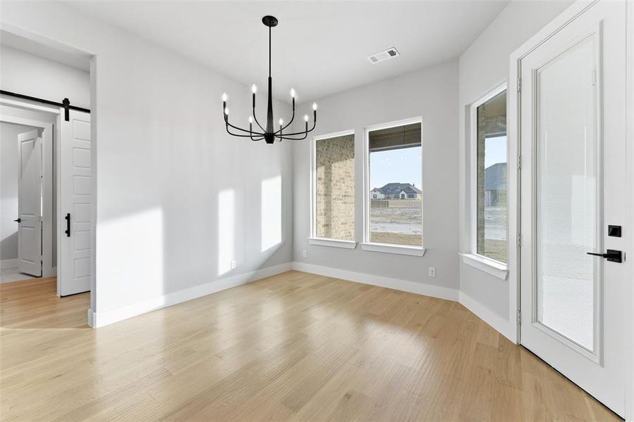 Unfurnished dining area featuring a barn door, light wood-style floors, and a chandelier