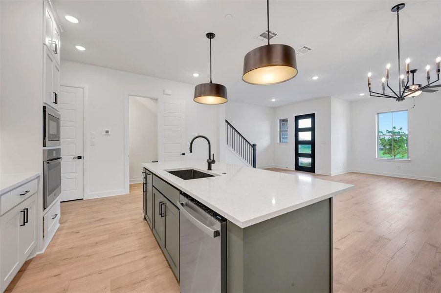 Open-concept kitchen featuring a spacious island with a countertop and built-in sink, stainless steel appliances, white cabinetry, and wood-finish flooring Open-concept kitchen featuring a spacious island with a countertop and built-in sink, stainless steel appliances, white cabinetry, and wood-finish flooring